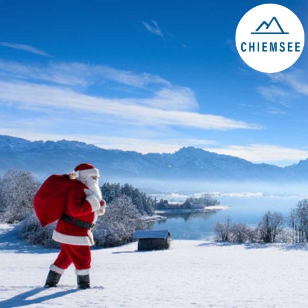 Der Weihnachtsmann spaziert vor verschneiter Bergkulisse am Chiemsee entlang